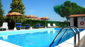 Zwembad met blauw water, omringd door witte ligbedden en gestreepte parasols.