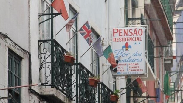Un immeuble d’habitation doté de balcons, une enseigne indiquant « PENSAO RESIDENCIAL Flor dos Galegos » et faisant la publicité de chambres, et une enseigne « ROMANO » en dessous.