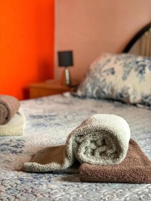 A neatly made bed with rolled towels and a patterned bedspread. - Pensão Residencial Flor dos Cavaleiros (Lisbon)