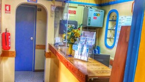 Un espace d’accueil avec un comptoir en bois, une porte bleue, un extincteur et un téléphone.