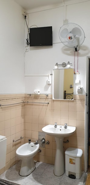 A bathroom with a white sink, bidet, and toilet, a mirror, a wall-mounted fan, and a television. - Pensão Residencial Flor dos Cavaleiros (Lisbon)