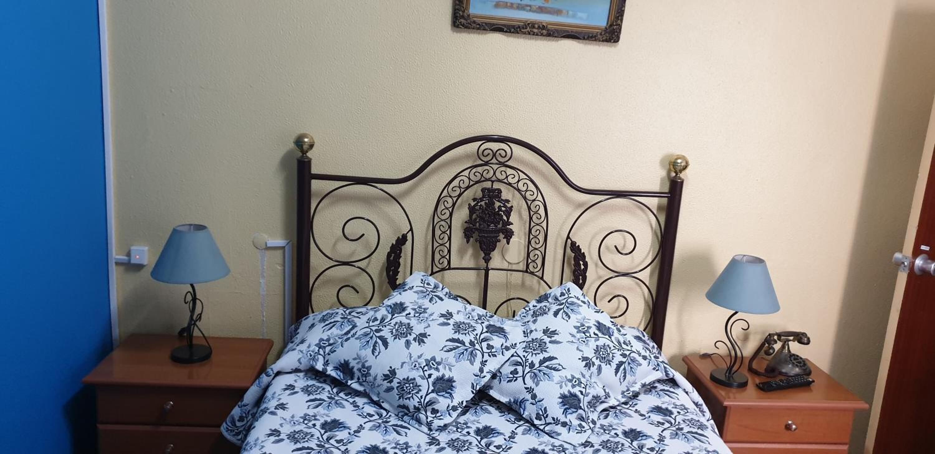A bed with a metal headboard, two bedside tables with lamps, and a framed picture on the wall.