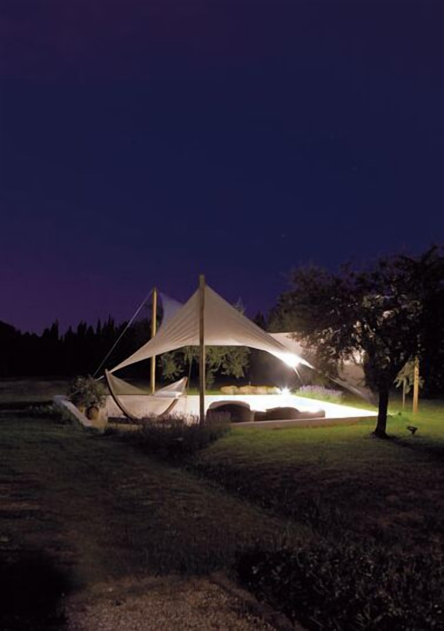 Eine zeltähnliche Struktur mit Baldachin, umgeben von einer grünen Wiese und Bäumen, bei Nacht.