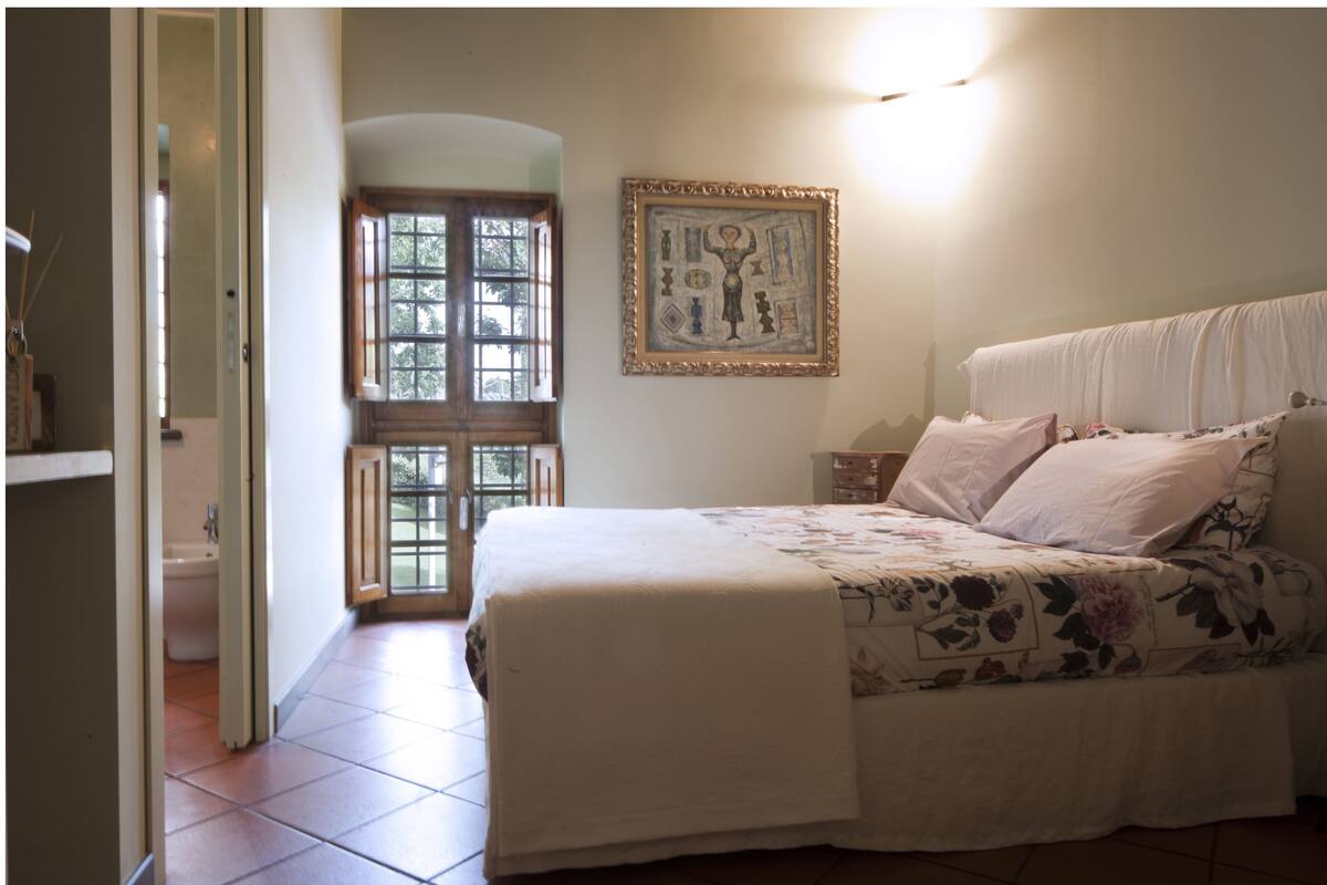 A bedroom with a bed, a window, a door, and a wall-mounted picture.