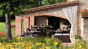 An outdoor dining area with brick arches, tables, and chairs, surrounded by a garden with yellow flowers. - La Casa di Rodo (Quarrata)