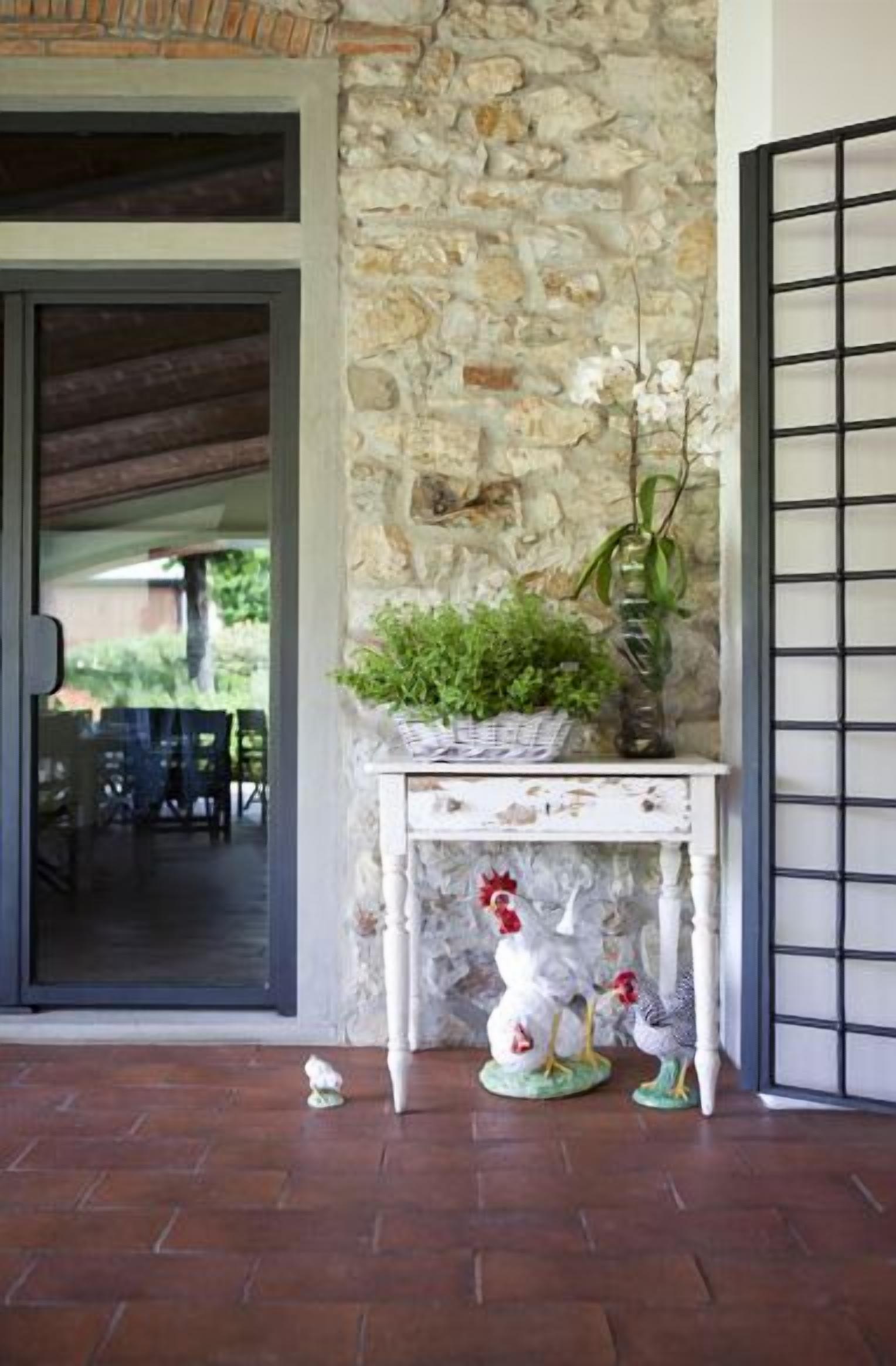 A stone wall, a white table with a plant and a rooster statue, and a door leading to an outdoor area.