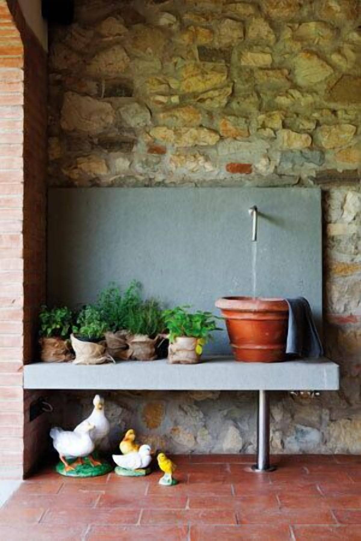 A stone wall with a shelf holding potted plants and a terracotta pot.