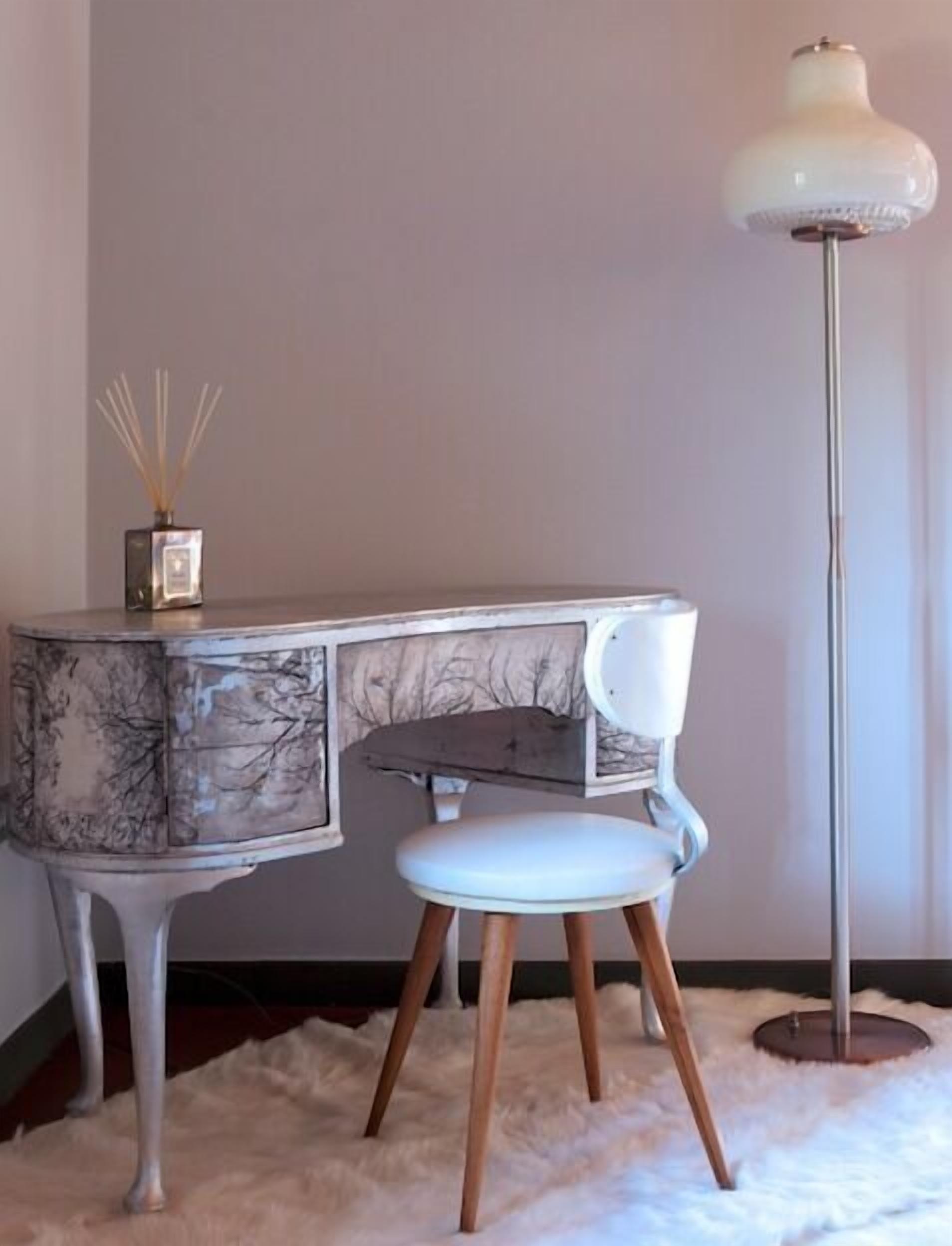 Un escritorio con diseño de mármol, una silla blanca y una lámpara de pie alta.