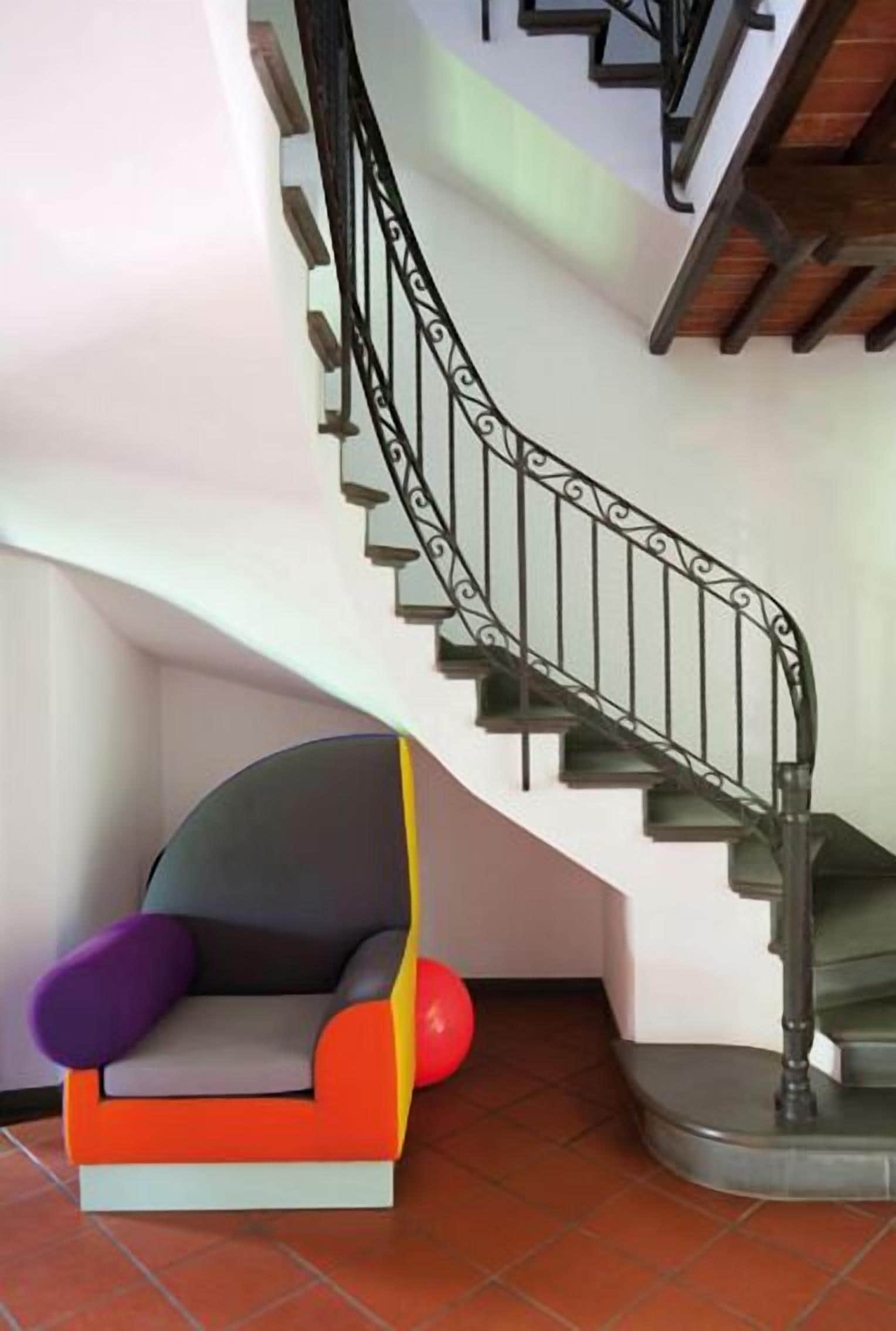 Uma escada com corrimão de metal preto e uma cadeira moderna com design colorido.