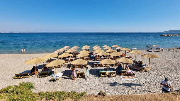 A beach with sun loungers and thatched umbrellas, a pebble beach, and the sea in the background. - Ilioxenia Studio & Apartments (Chios)