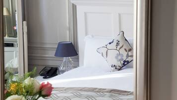 A hotel room with a bed, a bedside lamp, a telephone, and a floral arrangement.
