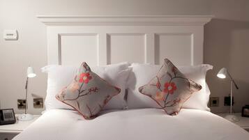 A neatly made bed with white bedding and two decorative pillows with floral designs.