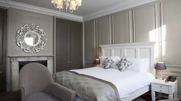 Quarto com uma cama grande, espelho, lareira, mesa de cabeceira e cadeira.