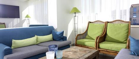 A living room with a blue sofa, a green armchair, a wooden coffee table, and a TV mounted on the wall.