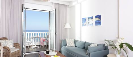 Ein Wohnzimmer mit einer Couch, einem Couchtisch mit Früchten, einem Korbsessel und Meerblick durch eine Glastür.