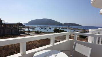 A balcony with a table and chairs, overlooking a marina with boats and a hilly landscape.