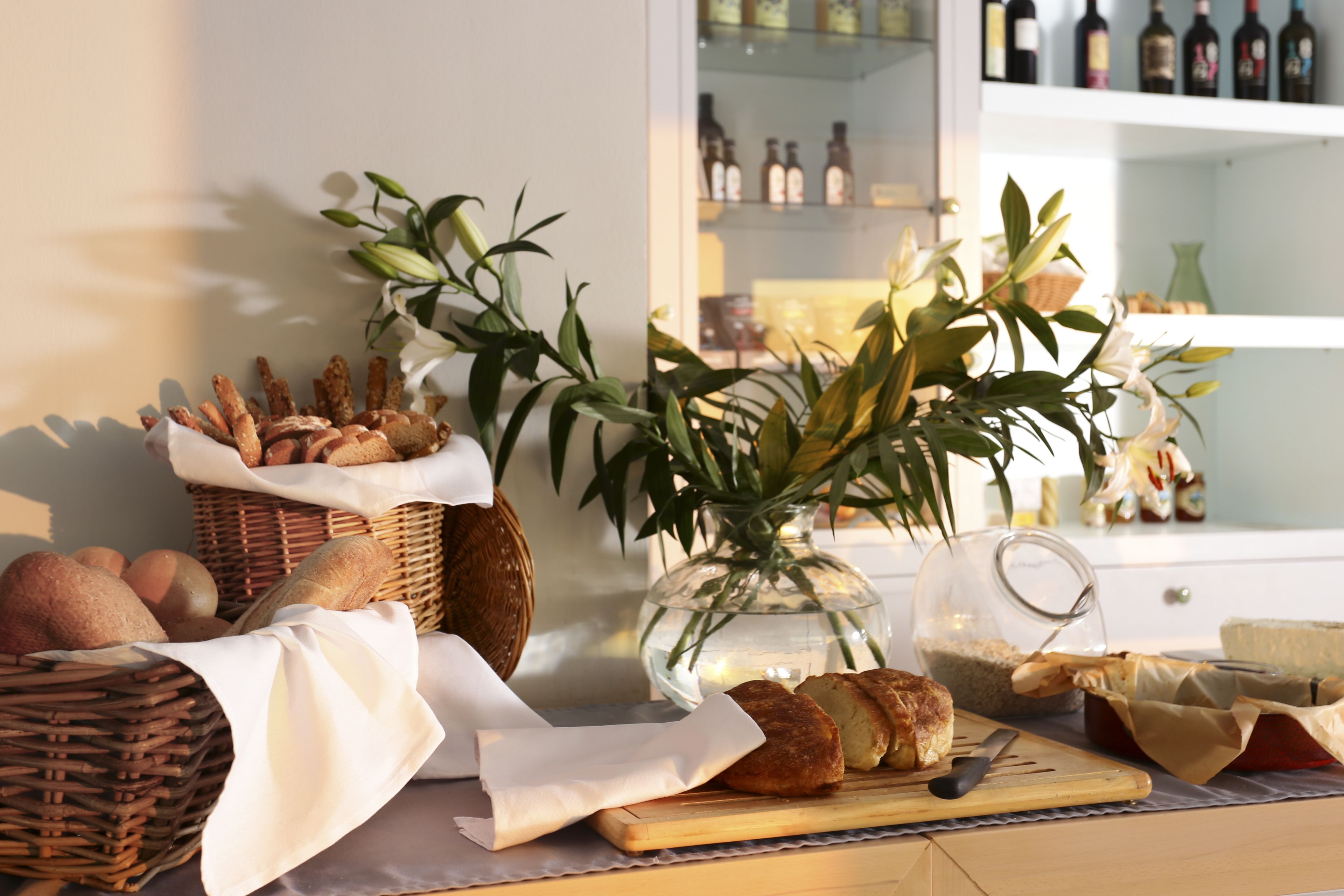 Un plan de travail de cuisine avec du pain, une planche à découper, un couteau et un vase rempli de fleurs.