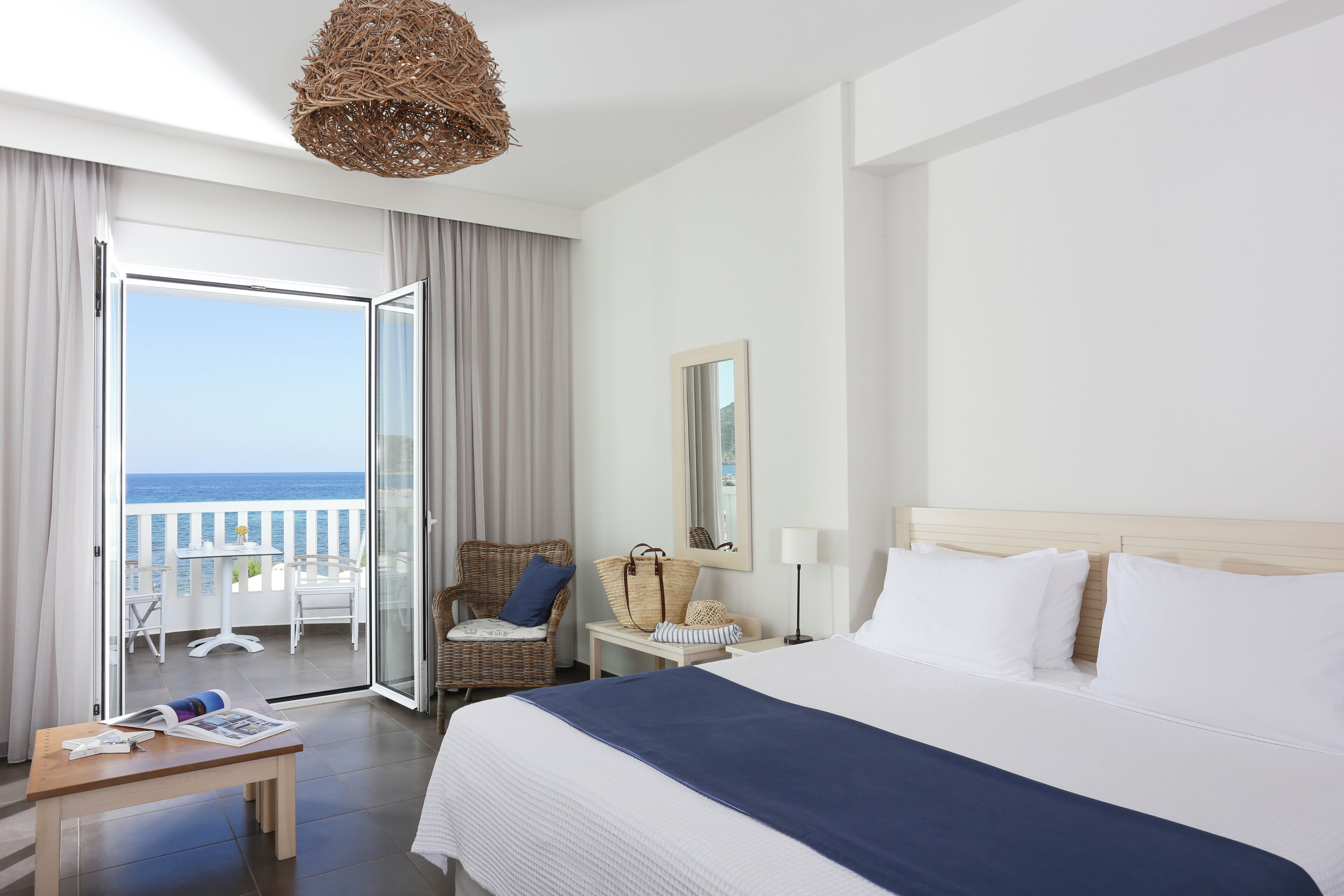 Ein Hotelzimmer mit Bett, Sessel, Tisch, Lampe und Meerblick.