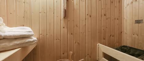 Un sauna de madera con un banco, un cubo y toallas en un estante.