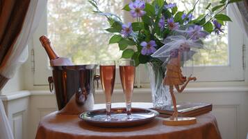 A table with a champagne bottle, two glasses, a vase with flowers, and a figurine.