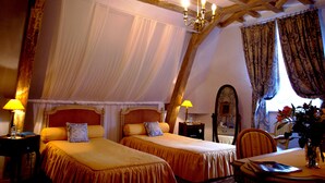Een slaapkamer met twee bedden, een kroonluchter, een houten plafond en een eethoek met een tafel en stoelen.