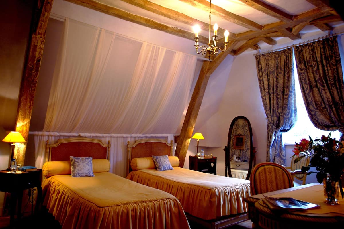 Ein Schlafzimmer mit zwei Betten, einer Kandelaber, einer Holzbalkendecke und einem Essbereich mit Tisch und Stühlen.