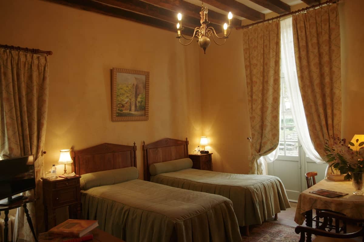 Ein Hotelzimmer mit zwei Betten, einer Kandelaber, einem Bild an der Wand und einem Fenster mit Vorhängen.
