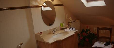 A bathroom with a skylight, a sink, a mirror, and a chair with a table.