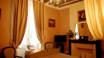 A hotel room with a bed, a desk with a television, a fireplace, and curtains.
