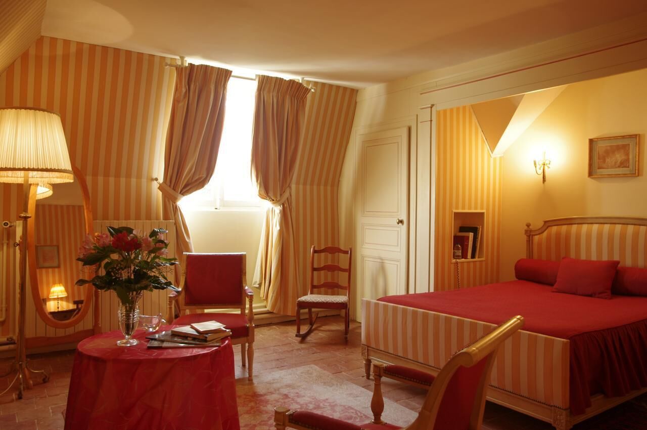 Une chambre d’hôtel avec un lit, une chaise, une table ornée d’un vase de fleurs et des rideaux.