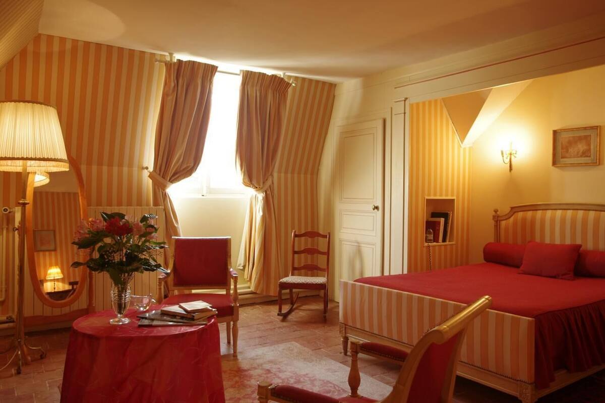 Ein Hotelzimmer mit Bett, Stuhl, Tisch und einer Blumenvase, sowie Vorhängen.