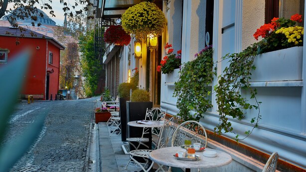 Una calle empedrada con mesas al aire libre, un edificio rojo y macetas de flores colgantes.