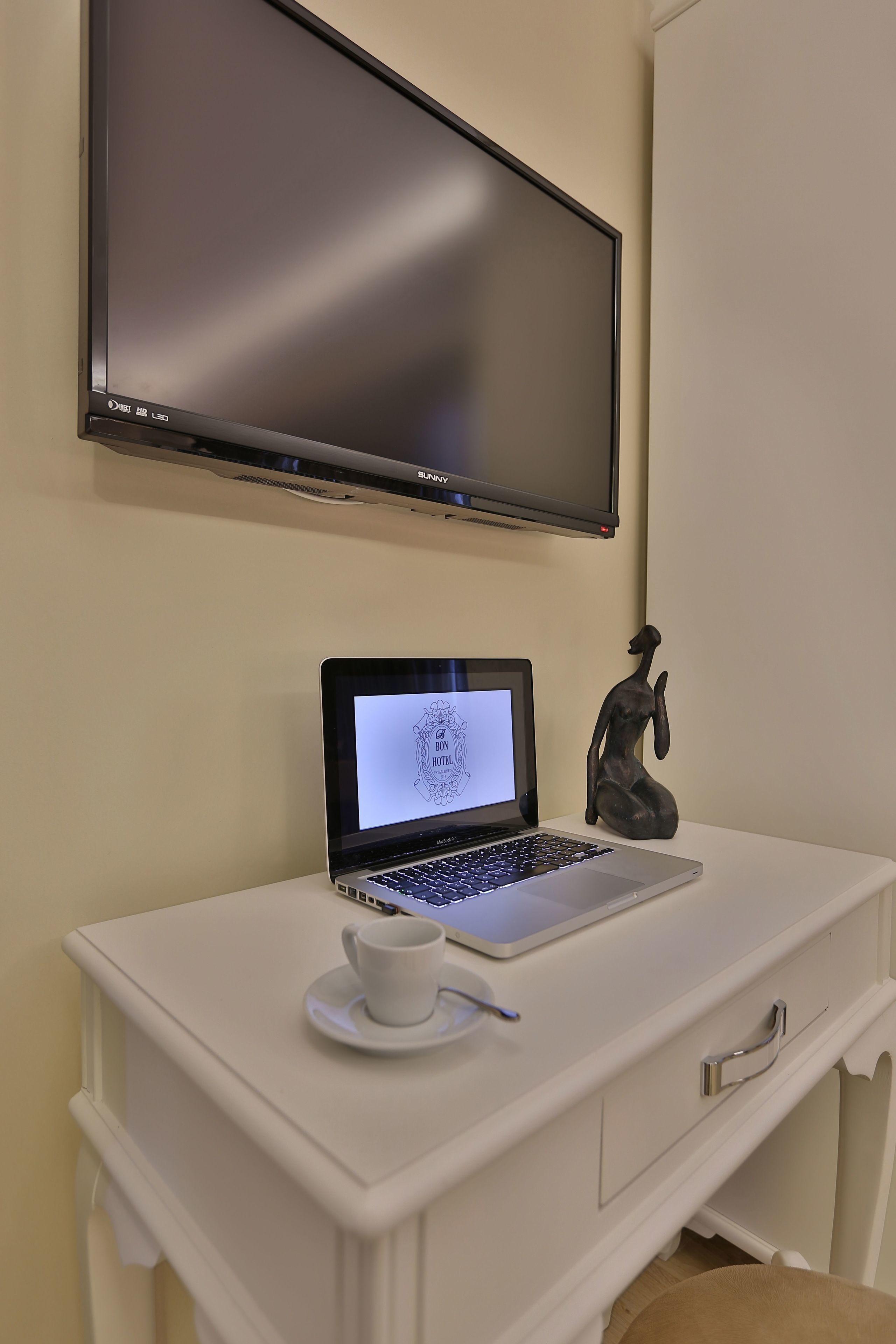 A white desk with a laptop, a cup, and a figurine.
