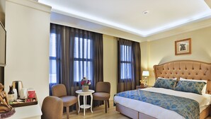 Una habitación de hotel con una cama grande, dos sillas, una mesita con un florero y un escritorio con una botella y una taza.