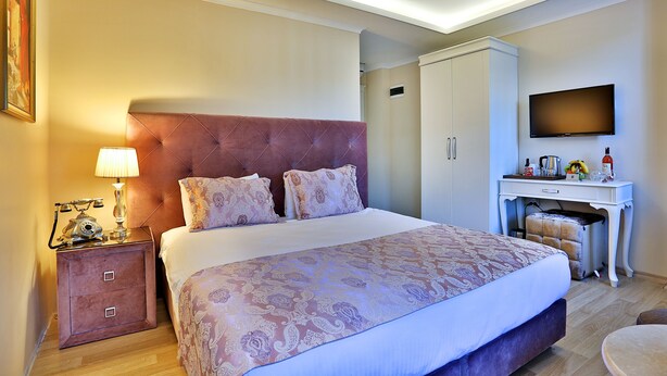 A hotel room with a large bed, a nightstand with a lamp, a wardrobe, a desk with a flat-screen TV, and a small round table. - Bon Hotel Hagia Sophia (Istanbul)
