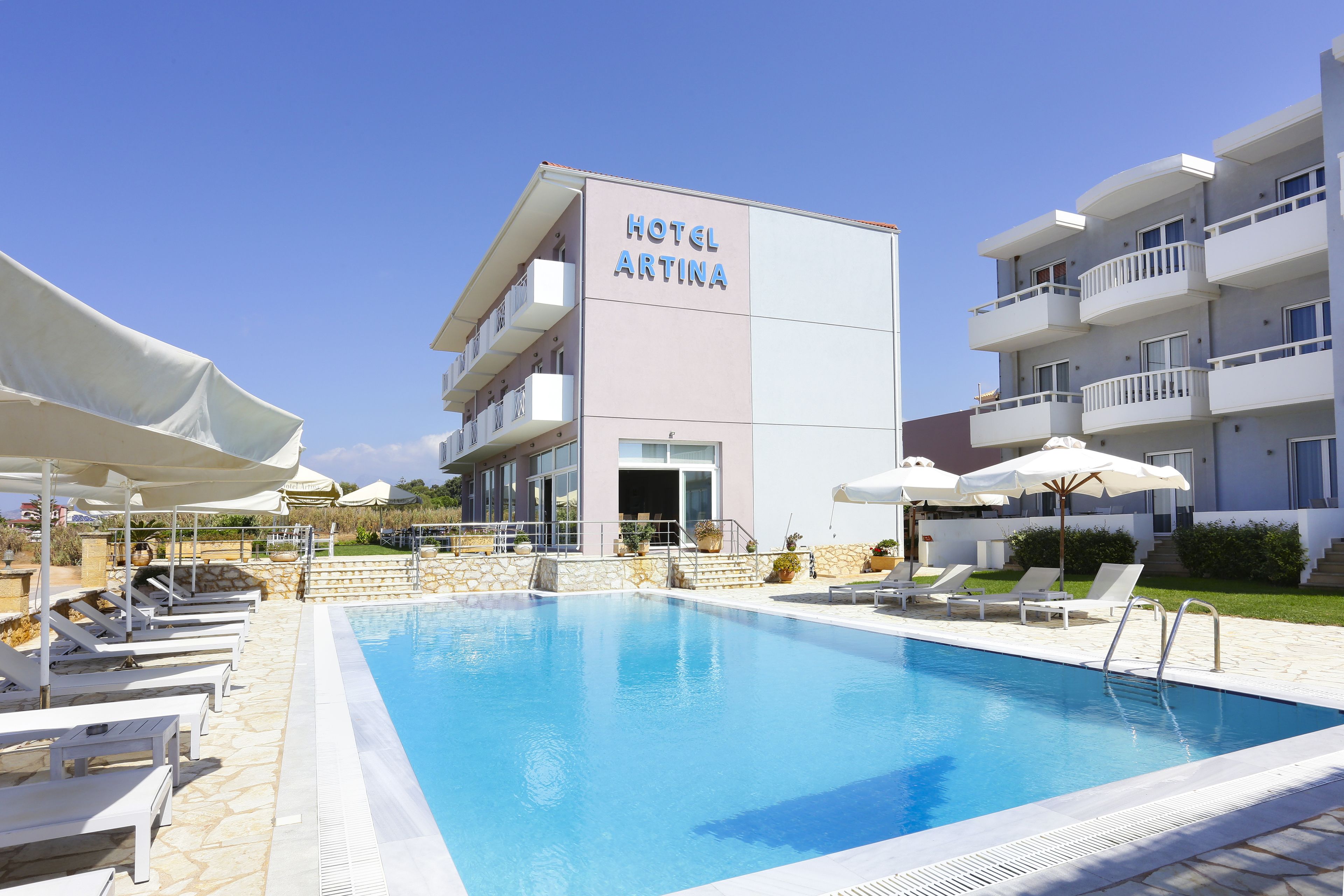 A hotel named 'HOTEL ARTINA' with a swimming pool, lounge chairs, and umbrellas.