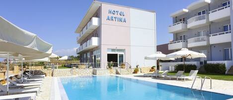 Un hotel llamado 'HOTEL ARTINA' con piscina, sillas de descanso y sombrillas.