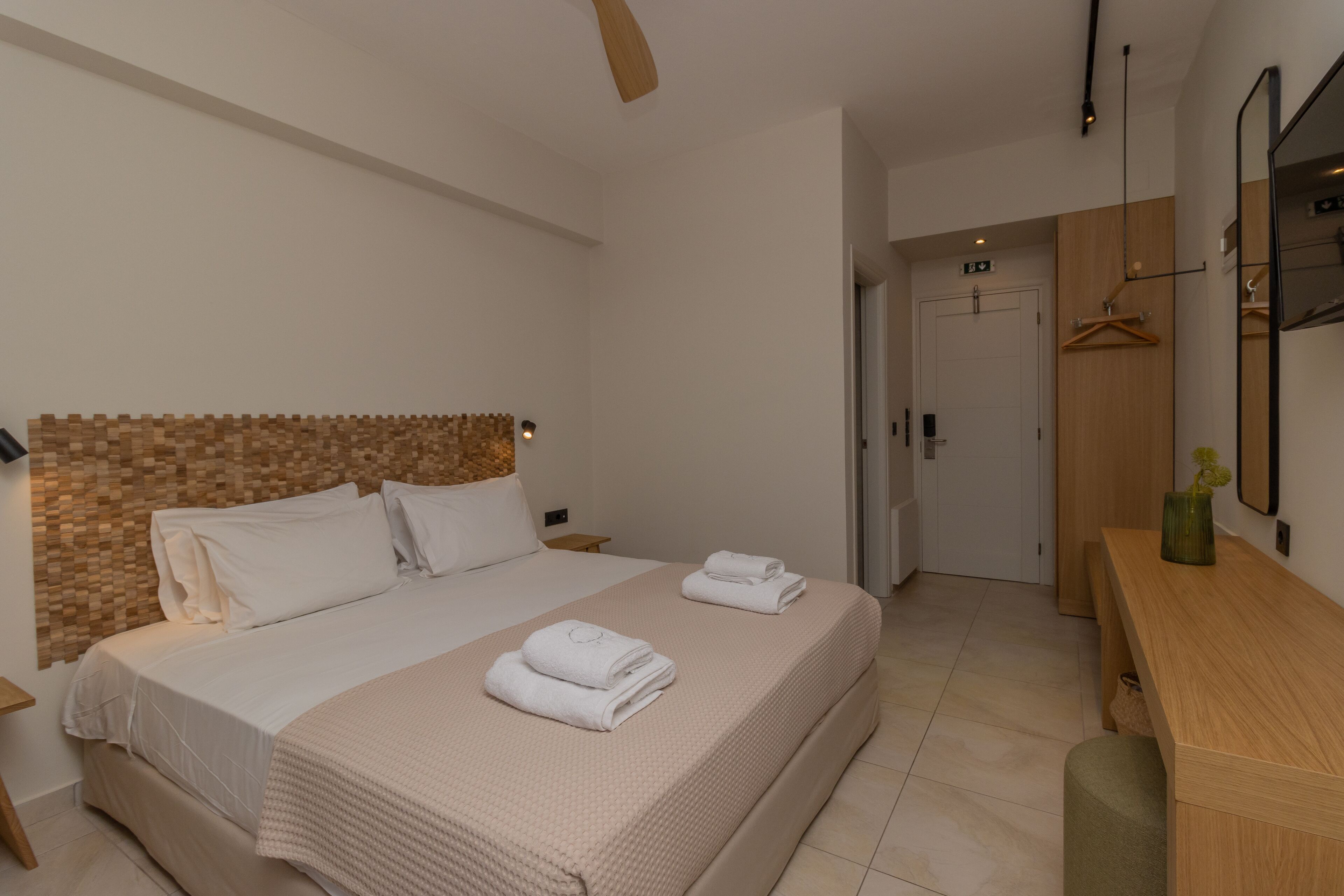 Una habitación de hotel moderna con una cama grande, cabecera de madera, mesita de noche, cómoda de madera y un espejo.