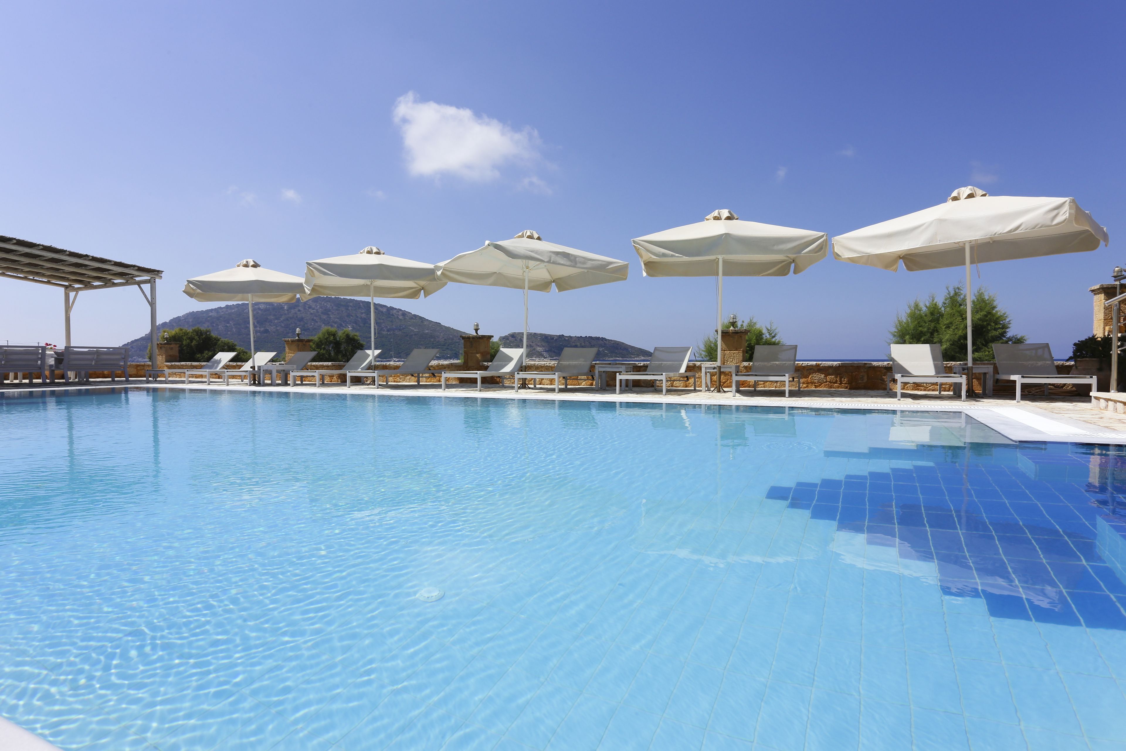 A swimming pool with lounge chairs and umbrellas, surrounded by mountains and clear skies.