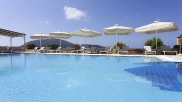 A swimming pool with lounge chairs and umbrellas, surrounded by mountains and clear skies.