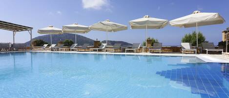 A swimming pool with lounge chairs and umbrellas, surrounded by mountains and clear skies.