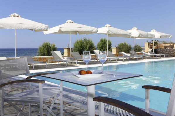 A poolside area with lounge chairs, umbrellas, and a table with glasses and fruit. - Artina Hotel (Trifylia)