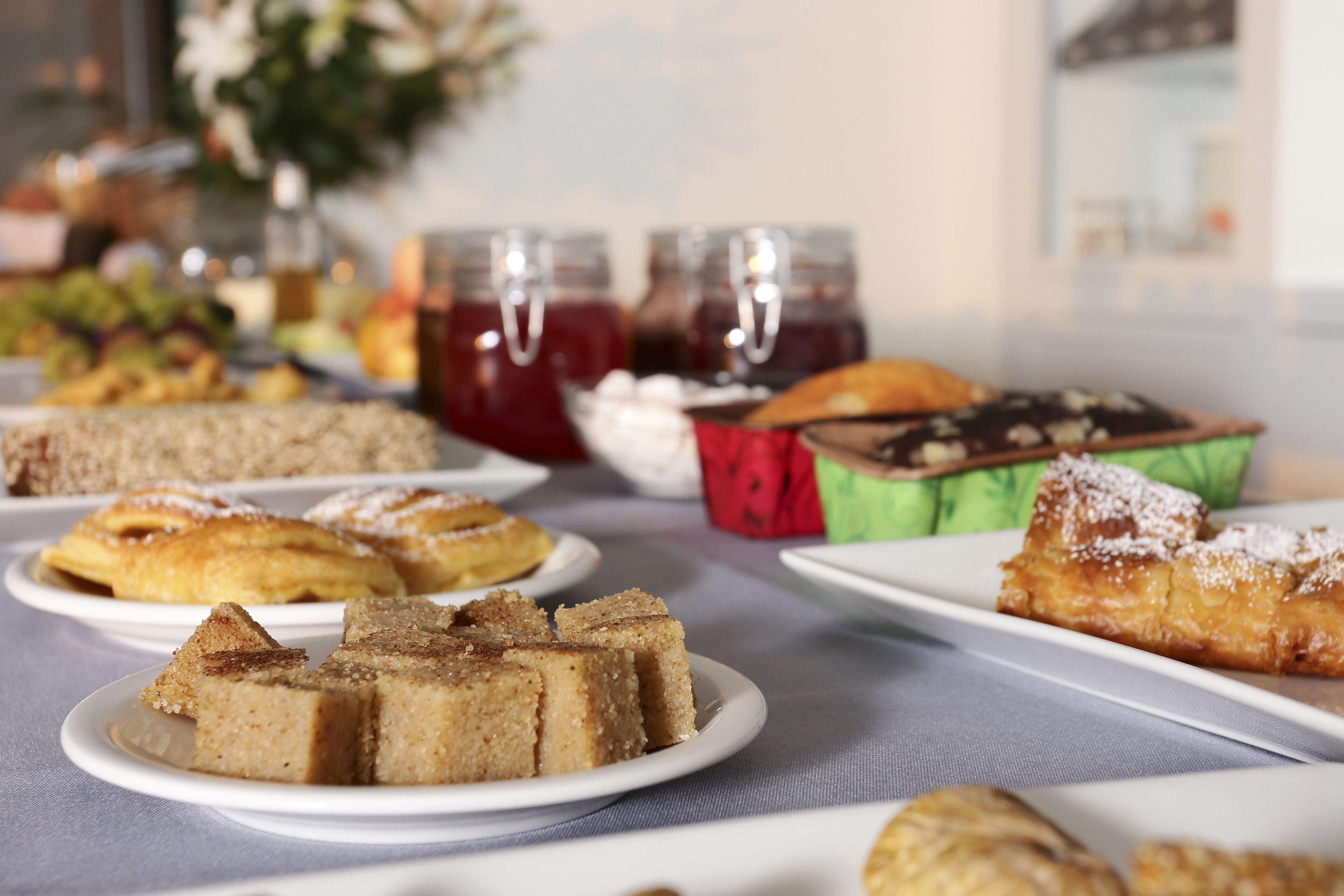Ein Tisch mit verschiedenen Desserts und Backwaren, darunter Kuchen und Kuchen, mit Gläsern Marmelade im Hintergrund.