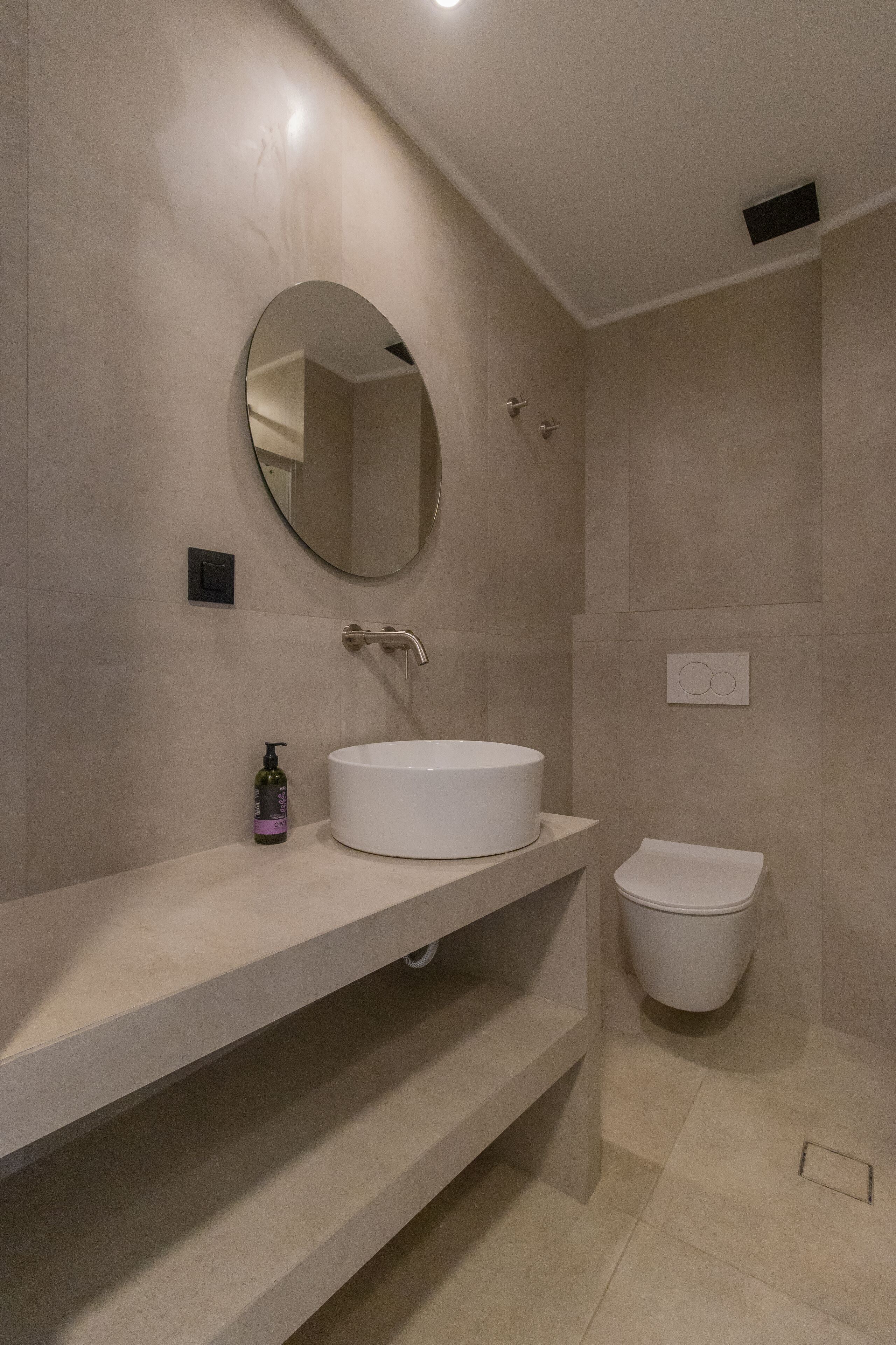 Een moderne badkamer met een ronde spiegel, een witte wastafel en een toilet.