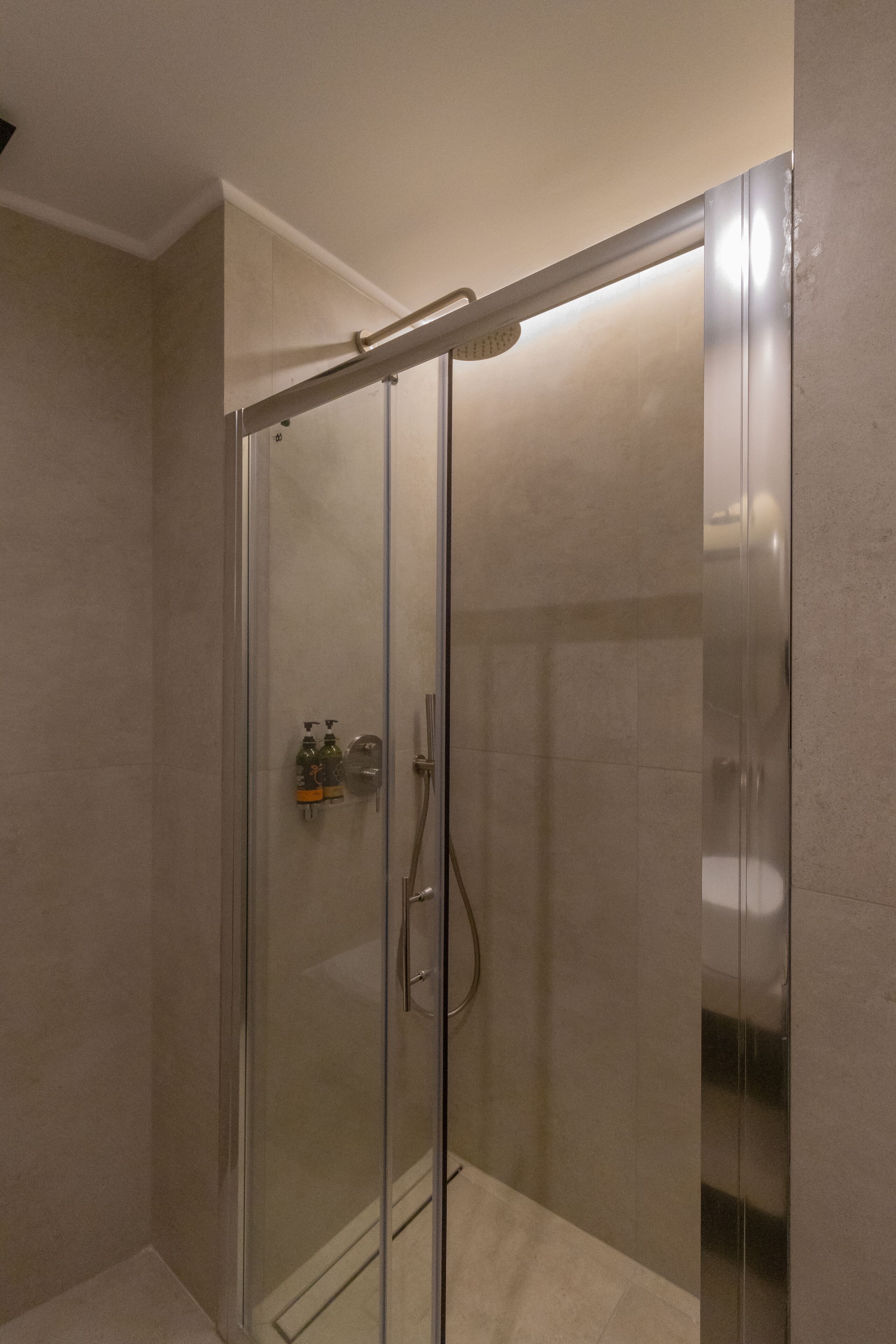 A glass-enclosed shower with a handheld showerhead and a wall-mounted faucet.