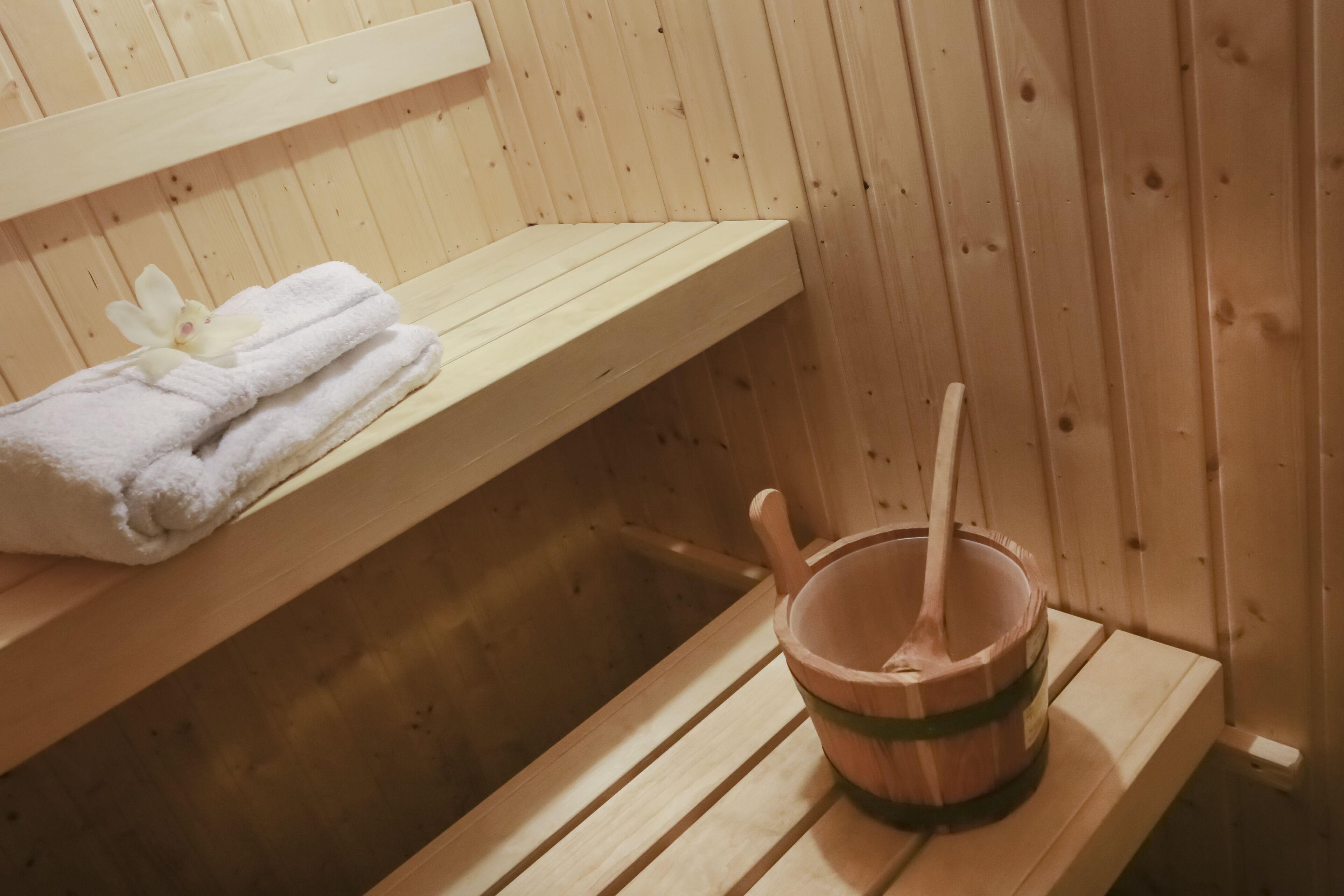 Een houten sauna met een bank, een handdoek en een houten emmer met een opscheplepel.