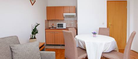 A compact living space with a kitchenette, a dining area with a table and chairs, a sofa, and a potted plant.