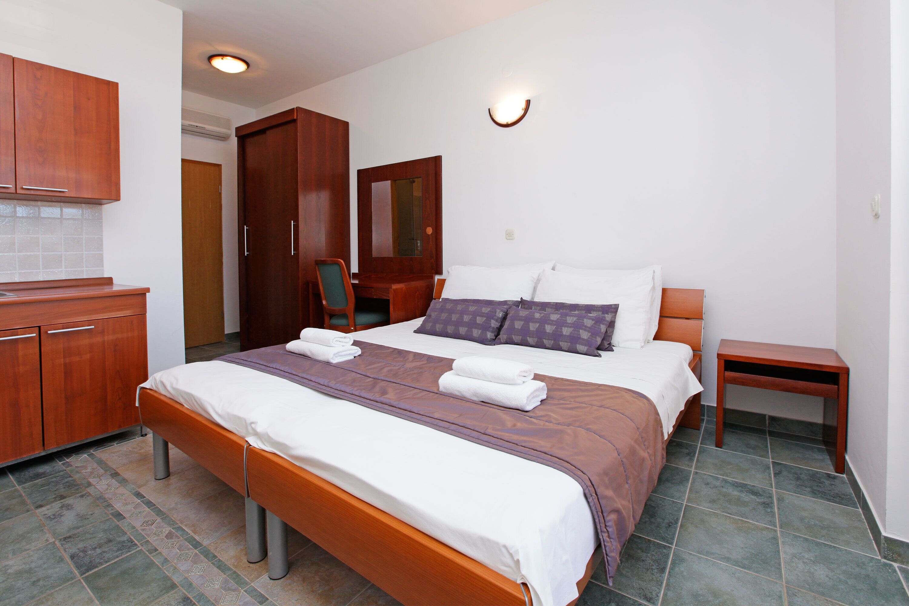 A neatly arranged hotel room with a bed, wooden furniture, a small table, and a mirror.