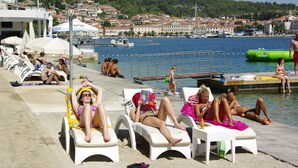 A poolside area with lounge chairs, a diving board, and a view of a town across the water. - Apartments Vala (Vela Luka)