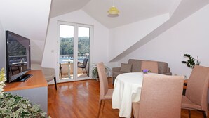 A modern living room with a wooden floor, a television, a sofa, a dining table with chairs, and a balcony with a view of greenery. - Apartments Vala (Vela Luka)